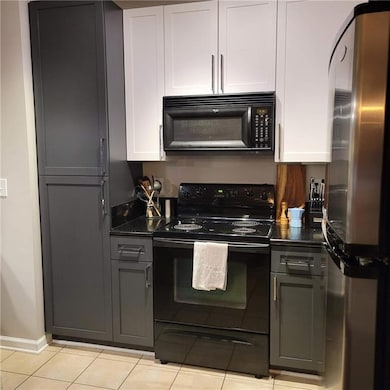 Kitchen with black appliances, light tile patterned floors, white cabinetry, and dark stone countertops