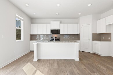 Kitchen with appliances with stainless steel finishes, an island with sink, backsplash, light wood-style flooring, and white cabinets