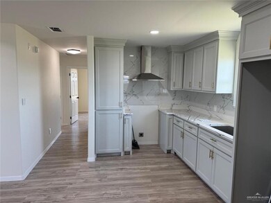 Kitchen featuring wall chimney range hood, backsplash, light wood finished floors, recessed lighting, and light stone countertops