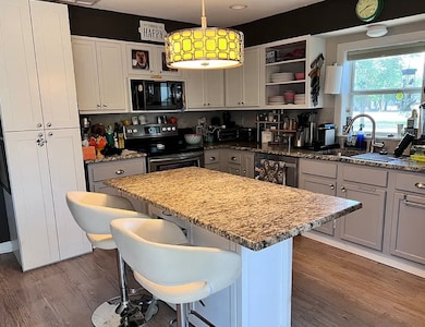 Kitchen featuring range with electric stovetop, white cabinetry, a center island, and light stone countertops