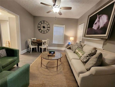 Living area with a textured ceiling, baseboards, a ceiling fan, and light wood-style flooring