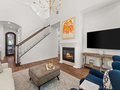 Living room featuring arched walkways, a glass covered fireplace, wood finished floors, a chandelier, and a towering ceiling