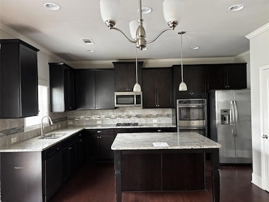 Kitchen featuring stainless steel appliances, a center island, dark wood finished floors, light stone countertops, and backsplash