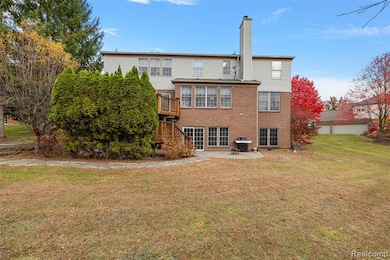 Back of house featuring a yard, a patio area, a chimney, brick siding, and a wooden deck