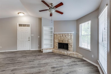 Unfurnished living room featuring a ceiling fan, wood finished floors, a fireplace, and vaulted ceiling