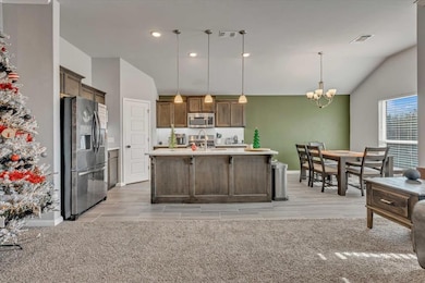 Kitchen with decorative light fixtures, stainless steel appliances, a chandelier, vaulted ceiling, and backsplash