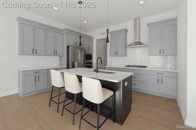 Kitchen with hanging light fixtures, gray cabinetry, a breakfast bar, an island with sink, and wall chimney exhaust hood