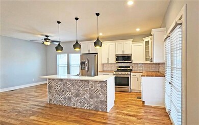 Kitchen with pendant lighting, tasteful backsplash, an island with sink, white cabinets, and stainless steel appliances