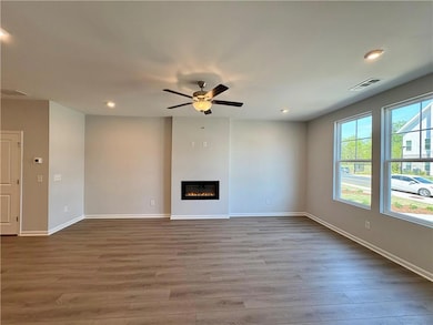 Unfurnished living room featuring a glass covered fireplace, baseboards, visible vents, ceiling fan, and wood finished floors