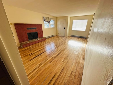 Unfurnished living room featuring a baseboard radiator, wood finished floors, and a fireplace