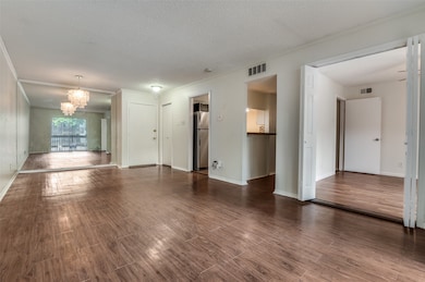 Unfurnished living room with crown molding, dark wood-type flooring, a chandelier, and a textured ceiling