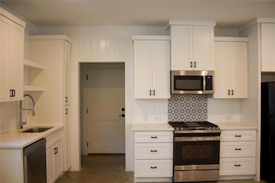 Kitchen featuring stainless steel appliances, open shelves, white cabinets, light stone countertops, and finished concrete flooring