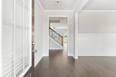 Entryway with a wainscoted wall, a decorative wall, crown molding, stairs, and dark wood finished floors