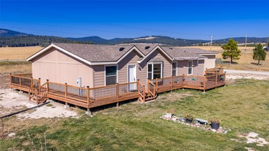 View of house with a deck with mountain view, roof with shingles, and a lawn
