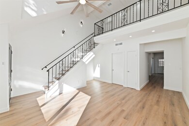 Open living space features high ceilings, a stylish staircase with wrought iron railing. The room is bathed in natural light, creating a welcoming and airy atmosphere.