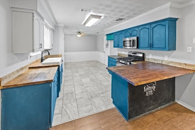 Kitchen with butcher block countertops, blue cabinets, crown molding, appliances with stainless steel finishes, and a peninsula