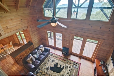 Living room with french doors, wood walls, a ceiling fan, high vaulted ceiling, and wood finished floors