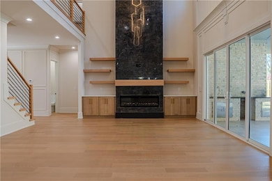 Unfurnished living room with stairway, a fireplace, light wood-style floors, recessed lighting, and a high ceiling