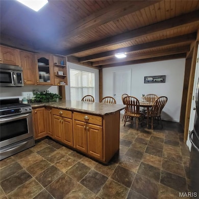Kitchen featuring a peninsula, stainless steel appliances, brown cabinetry, open shelves, and beam ceiling