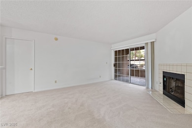 Unfurnished living room with carpet flooring, a textured ceiling, and a tile fireplace
