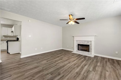 Unfurnished living room featuring a ceiling fan, dark wood-style flooring, a textured ceiling, and a high end fireplace