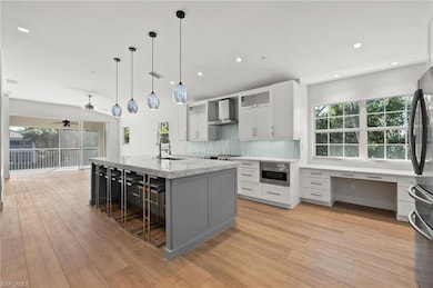 Kitchen with wall chimney exhaust hood, plenty of natural light, decorative backsplash, freestanding refrigerator, and recessed lighting