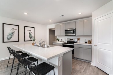 Kitchen featuring stainless steel appliances, gray cabinets, a kitchen breakfast bar, a kitchen island with sink, and light countertops