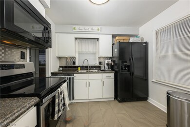 Kitchen featuring tasteful backsplash, white cabinetry, sink, and black appliances