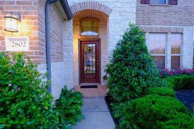 Covered entry surrounded by lush landscape.