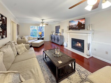 Living area featuring a ceiling fan, wood finished floors, ornamental molding, and a fireplace with flush hearth