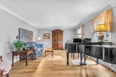 Sitting room with a textured ceiling, ornamental molding, light wood finished floors, and baseboards