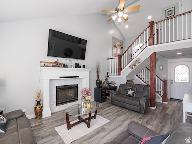 Living area with a fireplace, wood finished floors, high vaulted ceiling, stairs, and recessed lighting