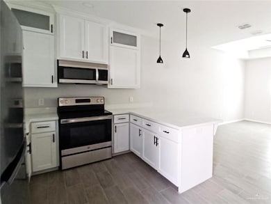 Kitchen with stainless steel appliances, glass insert cabinets, a peninsula, and white cabinetry