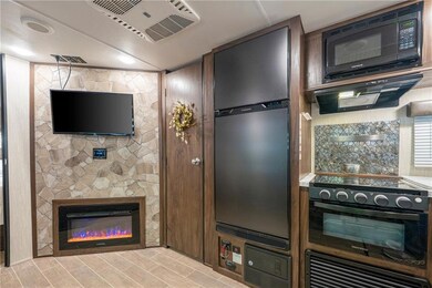 Kitchen with black appliances, exhaust hood, a glass covered fireplace, and light wood finished floors