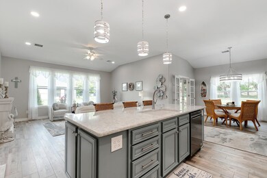 Kitchen featuring pendant lighting, an island with sink, light stone countertops, light wood-style floors, and gray cabinets