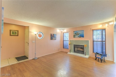 Living room with light wood-style floors, a textured ceiling, and a fireplace with raised hearth