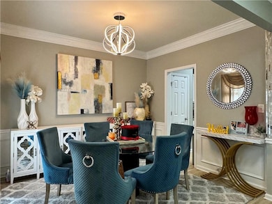 Dining room featuring crown molding, a wainscoted wall, a chandelier, wood finished floors, and a decorative wall