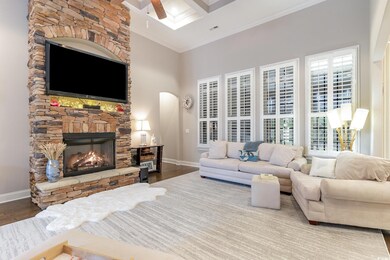 Living area with a high ceiling, ceiling fan, a fireplace, crown molding, and wood finished floors