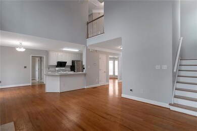 Unfurnished living room featuring a high ceiling, baseboards, wood finished floors, and stairway