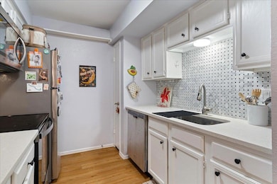 Kitchen featuring stainless steel appliances, white cabinets, backsplash, light wood finished floors, and light stone counters