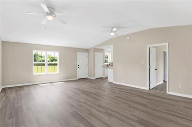 Unfurnished living room featuring a ceiling fan, lofted ceiling, plenty of natural light, wood finished floors, and baseboards