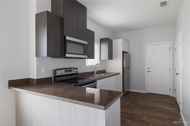 Kitchen with stainless steel appliances, sink, dark wood-type flooring, kitchen peninsula, and dark stone countertops