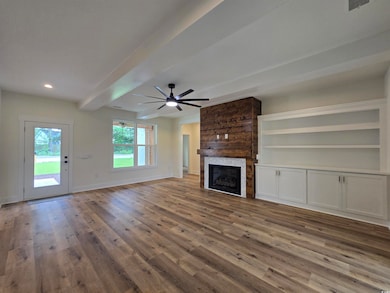 Unfurnished living room with beamed ceiling, a gas fireplace, ceiling fan, LVP floors, and custom built-ins.