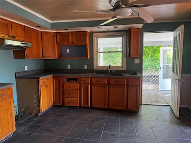 Kitchen featuring under cabinet range hood, ceiling fan, dark countertops, brown cabinets, and crown molding