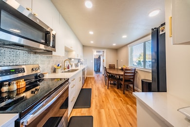 Kitchen with stainless steel appliances, light wood-style floors, white cabinets, light stone countertops, and recessed lighting