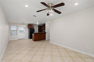 Kitchen featuring pendant lighting, ceiling fan with notable chandelier, and black refrigerator