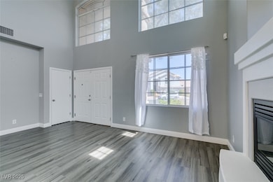 Unfurnished living room with a glass covered fireplace, a towering ceiling, and wood finished floors