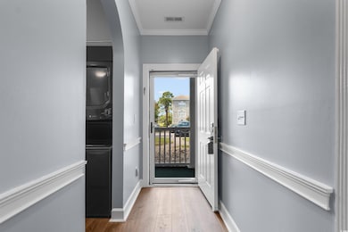 Doorway with crown molding, wood finished floors, stacked washer / dryer, and arched walkways