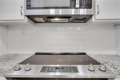 Kitchen with appliances with stainless steel finishes, backsplash, white cabinetry, and light stone countertops