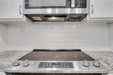 Kitchen with appliances with stainless steel finishes, backsplash, white cabinetry, and light stone countertops